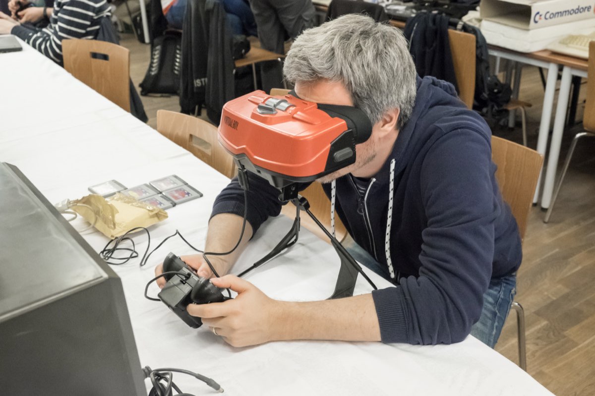Una persona inclinada sobre una Virtual Boy apoyada en su pie, sobre una mesa, con el mando en las manos